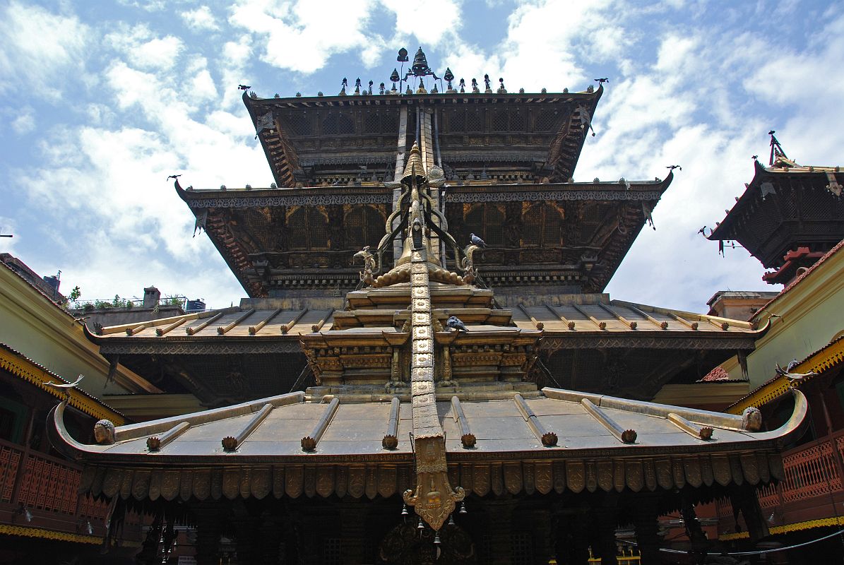 Kathmandu Patan Golden Temple 07 Main Temple With Swayambhu Chaitya In Front The large rectangular Golden Temple in Patan has three roofs and a copper-gilded fa�ade. The long metal strips coming down from the roof are supposed to provide a slide for the gods when they descend to answer prayers. In the foreground is the roof of the Swayambhu Chaitya.